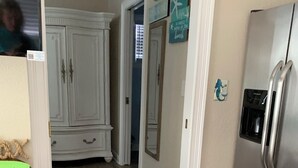 A kitchen with wooden flooring, white cabinets, a stainless steel refrigerator, and a green mat on a wooden stool. - SURF SHACK (Cape Canaveral)