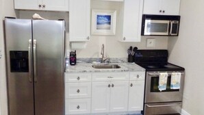 A kitchen with white cabinets, a stainless steel refrigerator, a microwave, and a stove. - SURF SHACK (Cape Canaveral)
