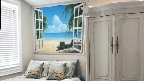 A bedroom with a beach view mural, a bed with patterned bedding, a white wardrobe, and wooden flooring. - SURF SHACK (Cape Canaveral)