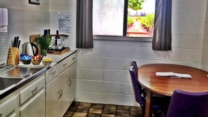 A small kitchen with a window, a sink, a wooden table, and a chair. - The Picker's Hut - Peaceful vineyard setting (Monash)
