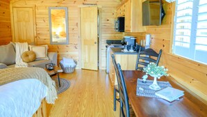 A cozy cabin with a wooden interior, a dining area with a table and chairs, a kitchen with a microwave, and a TV mounted on the wall. - 1 Queen size bed &Love seat sofa, Creek view (Shamokin)