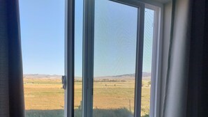 Une fenêtre donnant sur un champ verdoyant et des collines lointaines.