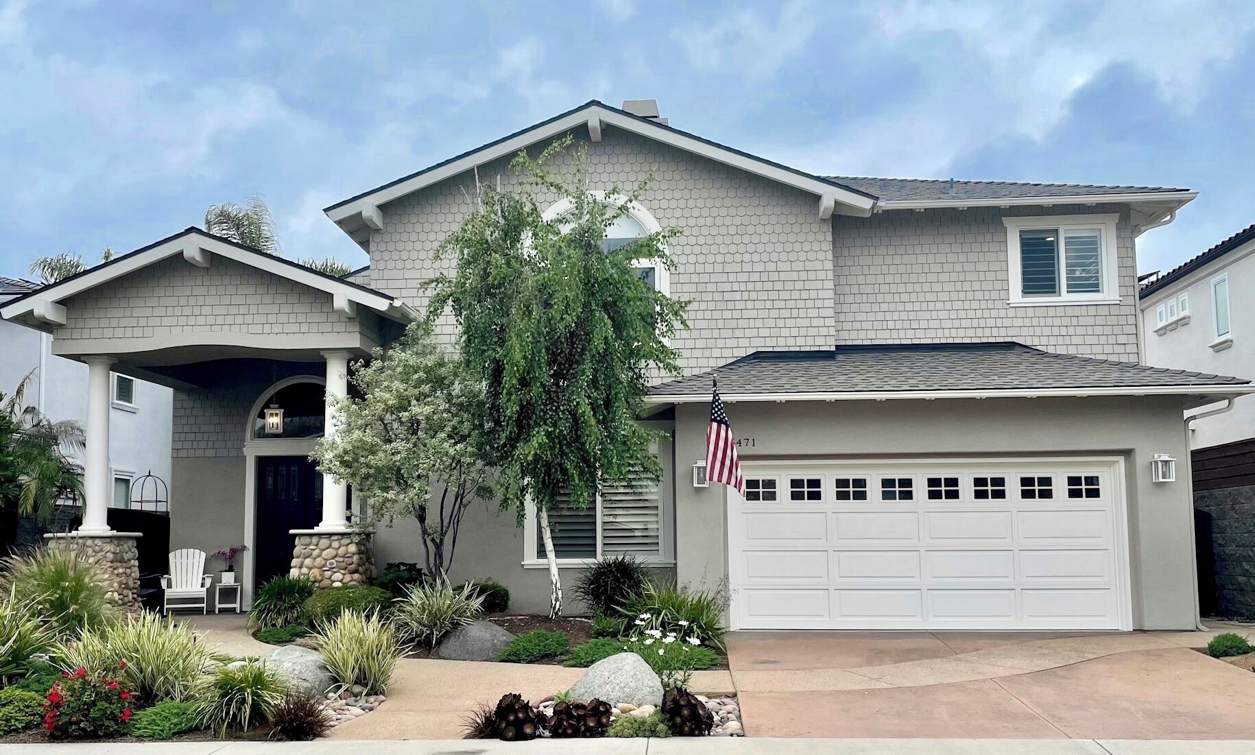A two-story house with a garage, a front porch, and a landscaped garden.
