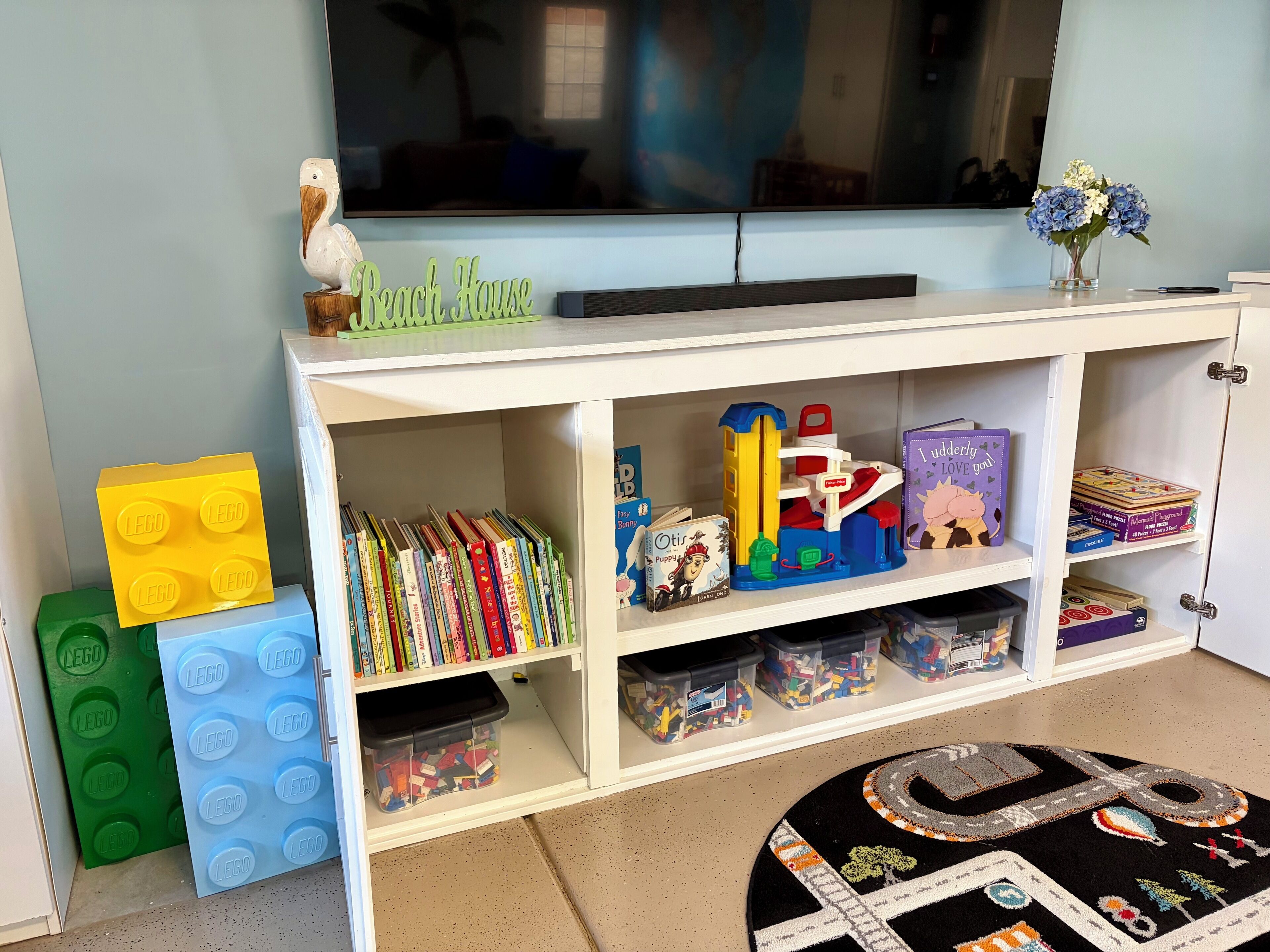 Un área de juegos infantiles con un estante blanco que contiene libros, juguetes y piezas de LEGO.