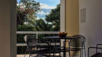 A balcony with a table and chairs, a bowl of fruit, and a view of trees and sky.