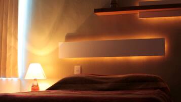 A modern hotel room with a bed, a bedside lamp, and wall-mounted shelves.