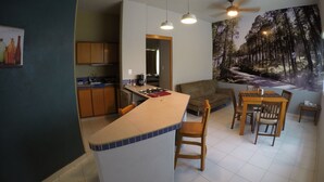 Een moderne keuken met een centraal eiland, een houten eettafel en stoelen. Op de muur bevindt zich een groot muurschildering van een boslandschap.