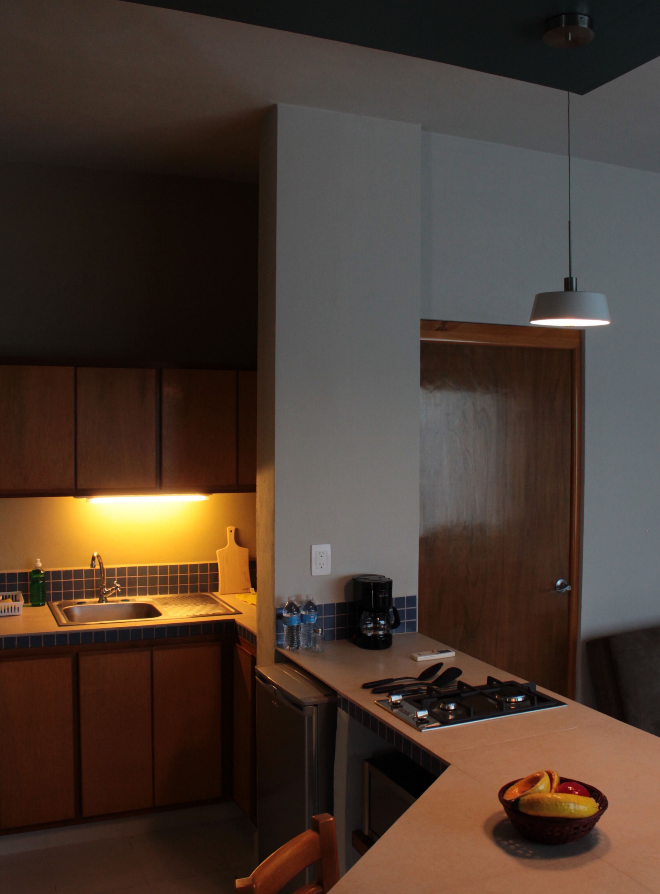 A kitchen with a sink, cabinets, a coffee maker, and a fruit bowl on the counter.