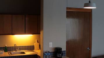 A kitchen with a sink, cabinets, a coffee maker, and a fruit bowl on the counter.