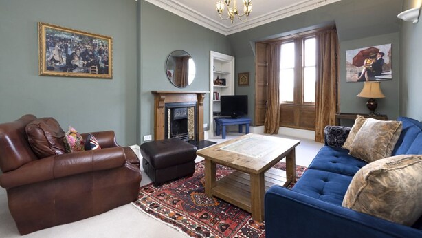 Un salon avec un canapé en cuir marron, un canapé bleu, une table basse en bois, une cheminée, un téléviseur et un grand miroir au mur.
