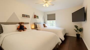 A hotel room with two beds, a ceiling fan, a TV, and a potted plant.
