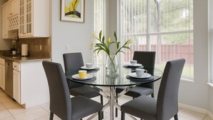 En matplats med ett glasbord omgivet av fyra stolar, en vas med blommor och en tavla på väggen.