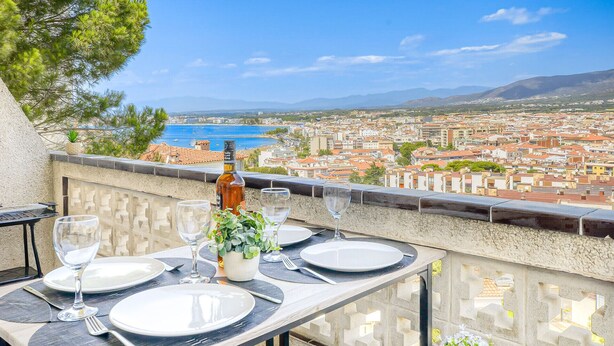 A table set for two with a bottle and glasses, overlooking a coastal cityscape.