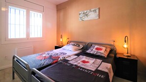 A bedroom with two beds, a radiator, a window, and wall-mounted lamps.