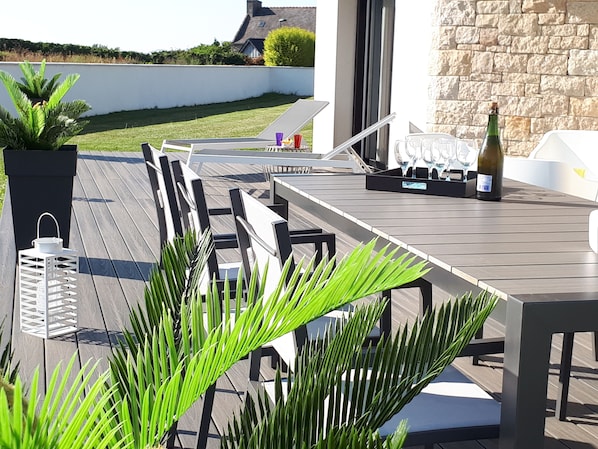 An outdoor patio with a wooden deck, seating area, and a table with a bottle and glasses.