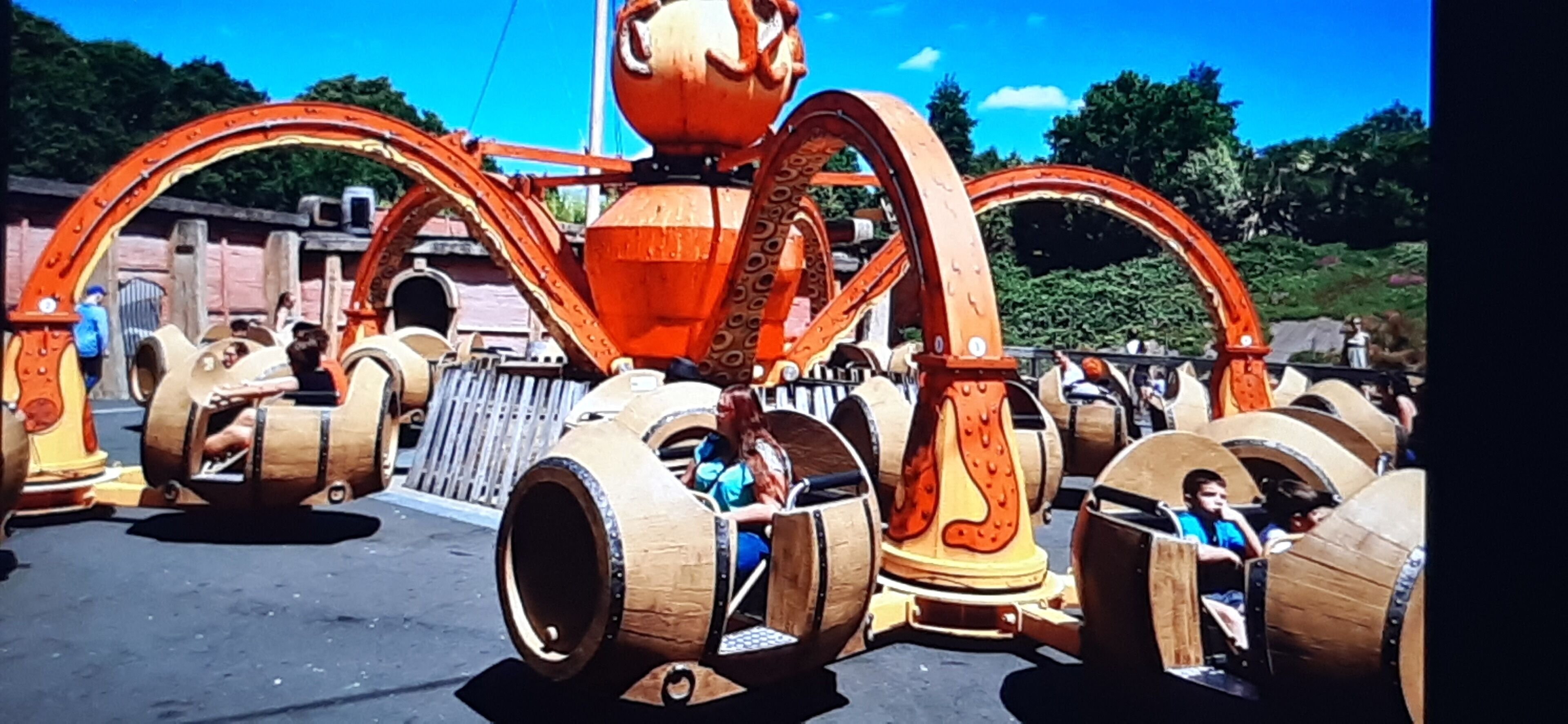 A mechanical ride with large wooden barrels and orange mechanical parts.