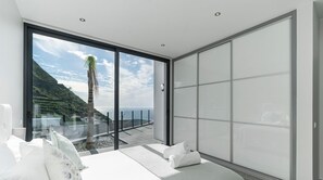 Enjoy a panoramic coastal view from the comfort of this stylish room, featuring a large bed and floor-to-ceiling windows.