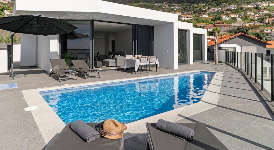 A modern outdoor pool area with lounge chairs, a dining table, and a large umbrella.