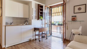 A modern kitchen with white cabinets, a wooden cart, and a glass door leading to a balcony. - Lago Terrione Apartment - Charme Holidays (Rome)