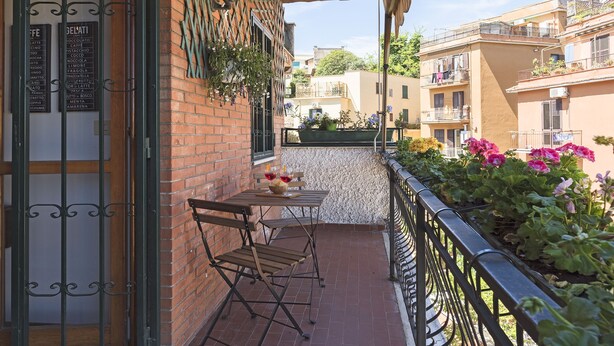 A balcony with a table and chairs, a menu board, and potted plants. - Lago Terrione Apartment - Charme Holidays (Rome)