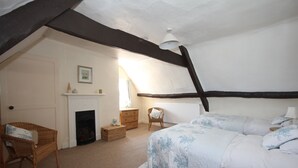 Ein Schlafzimmer mit schrägen Wänden, einem Kamin, einem Bett mit floralem Bettbezug und einem Korbstuhl.
