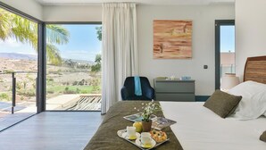 A hotel room with a bed, a desk, a chair, a painting, and a view of the desert landscape. -  Los Lagos 39 Salobre Golf (Maspalomas)