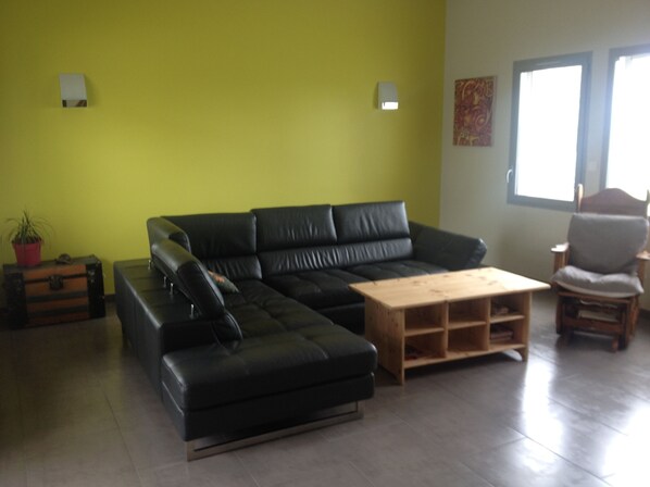 A living room with a black sectional sofa, a wooden coffee table, a wooden side table, a chair, and a potted plant. - Modern house located between sea and mountains, ideal for discovering the region (Saint-Pierre-D'irube)