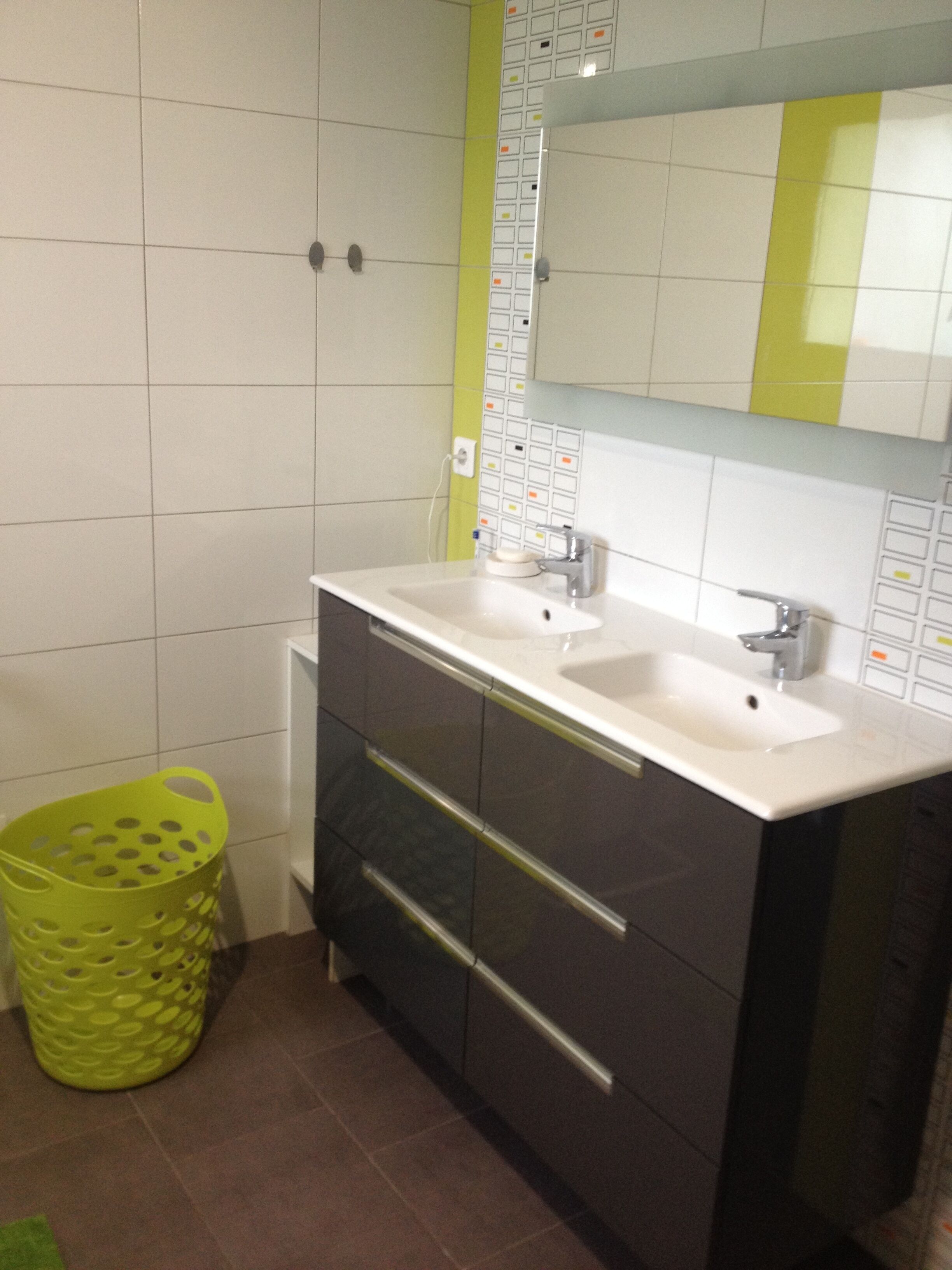 Un bagno con un lavandino bianco, due specchi e un cesto verde.