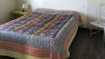 Een slaapkamer met een groot bed, een klein nachtkastje, een stoel en een houten plafond.