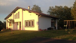 A two-story house with a flat roof, a chimney, and a swing set in the yard.