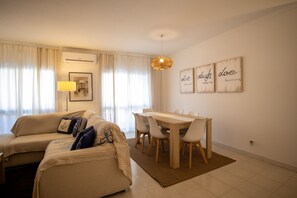 A modern living room with a sofa set, a dining table with chairs, and a hanging light fixture.