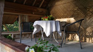 Un patio al aire libre con una mesa cubierta con un mantel blanco, dos sillas de metal y una maceta con flores rojas.