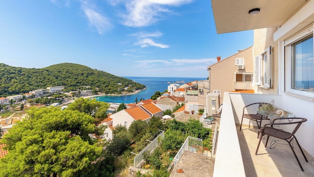 A balcony with a view of a coastal town, a swimming pool, and a hilly landscape.