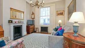A living room with a fireplace, a sofa, a television, and a chandelier. - Traditional 1 Bed Apartment, Pimlico (London)