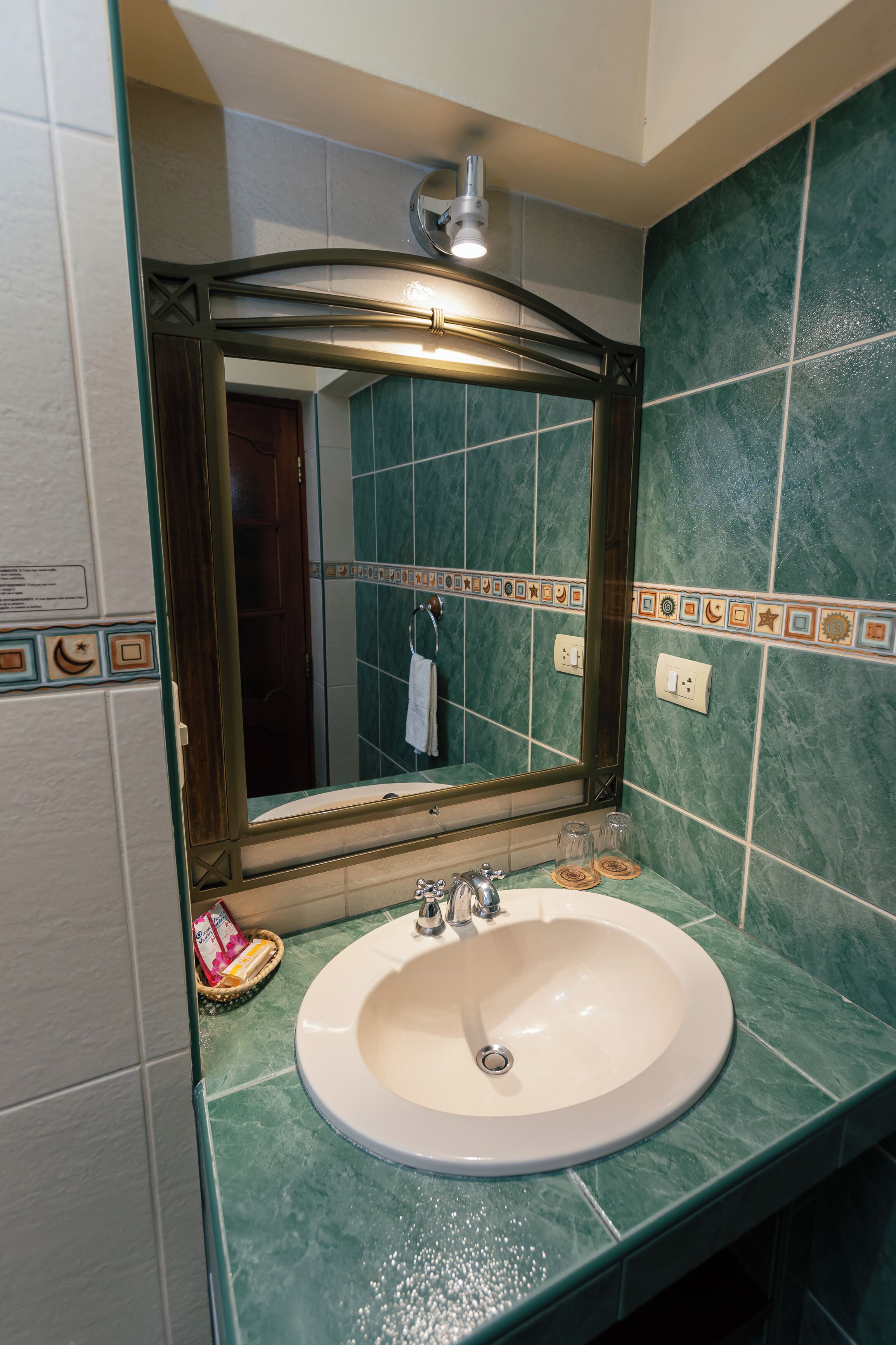 Ein Badezimmer mit Waschbecken in Weiß, grünen Marmorfliesen und einem Spiegel mit dekorativem Rahmen.