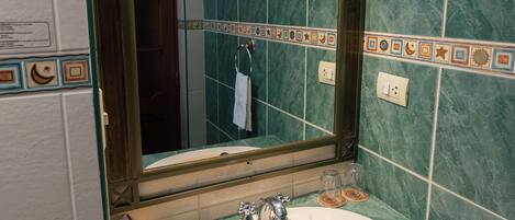 Une salle de bain avec un lavabo blanc, des carreaux de marbre vert et un miroir doté d’un cadre décoratif.