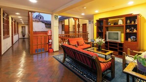 A traditional-style living room with a sofa, wooden furniture, and a television. - Amerindia Hotel (Cusco)