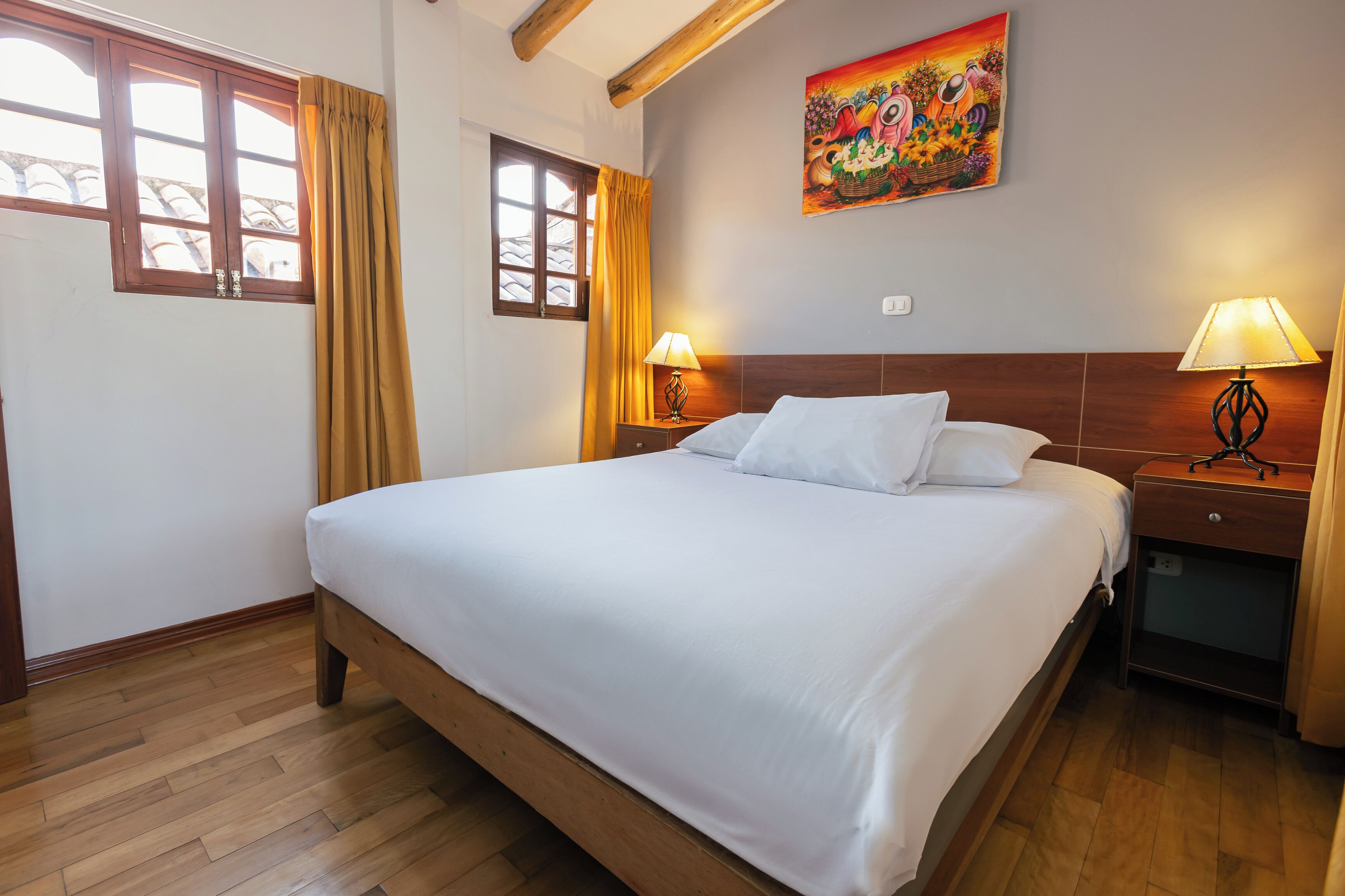 Une chambre d’hôtel avec un grand lit, un plancher en bois, deux lampes de chevet, un tableau au mur et une fenêtre avec des rideaux.