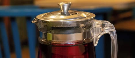 A clear glass teapot with a metal lid on a white saucer, placed on a wooden table.