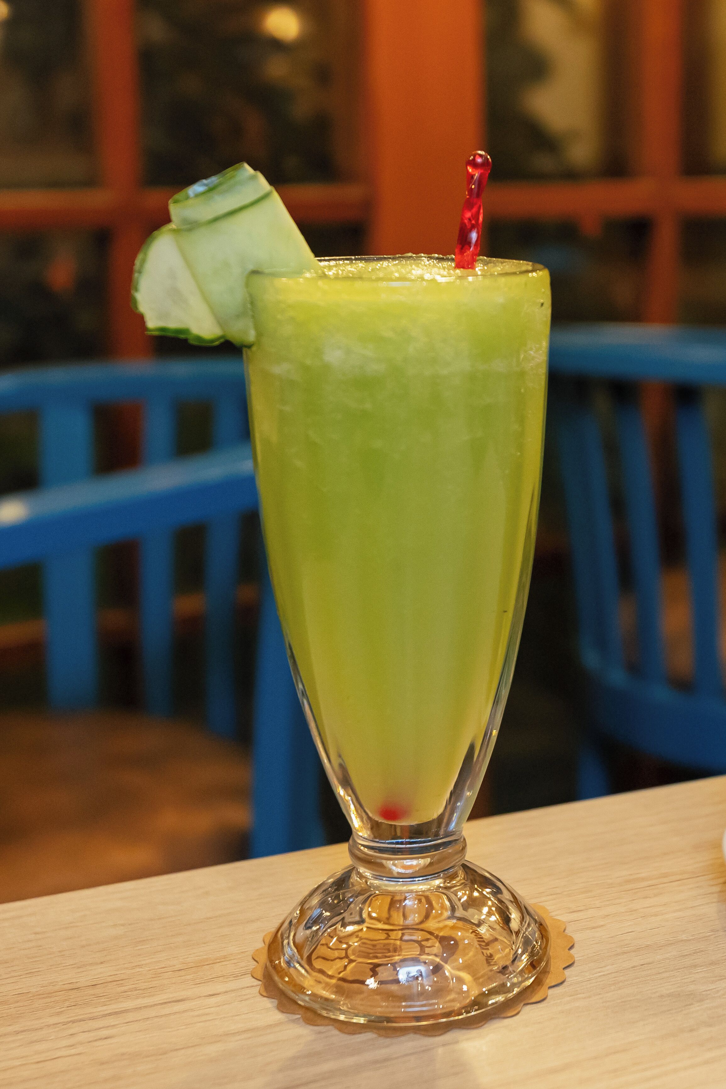 A tall glass with a green beverage, garnished with a slice of lime and a red straw, on a wooden table.