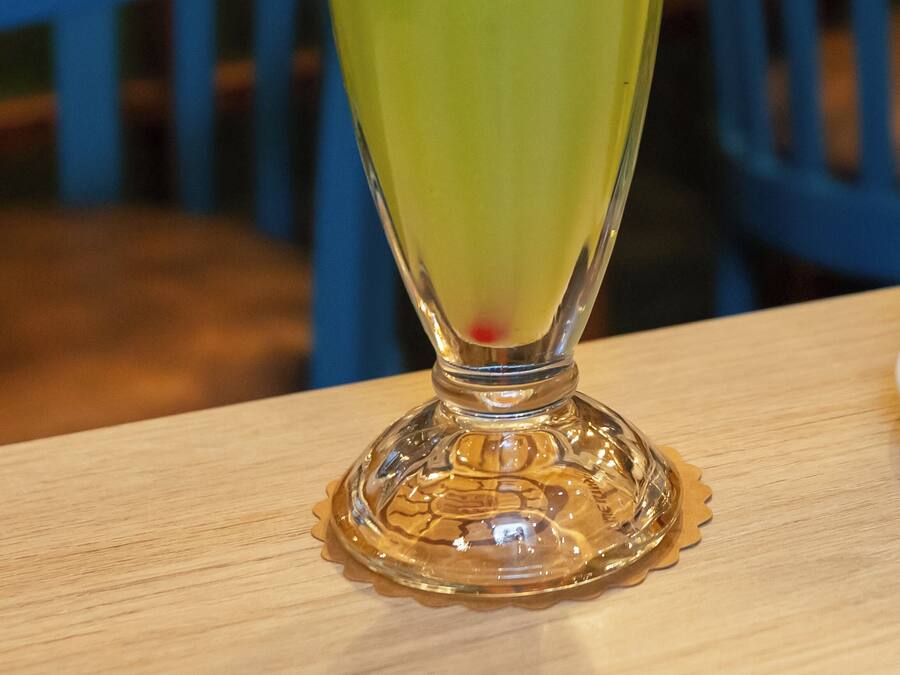 A tall glass with a green beverage, garnished with a slice of lime and a red straw, on a wooden table.