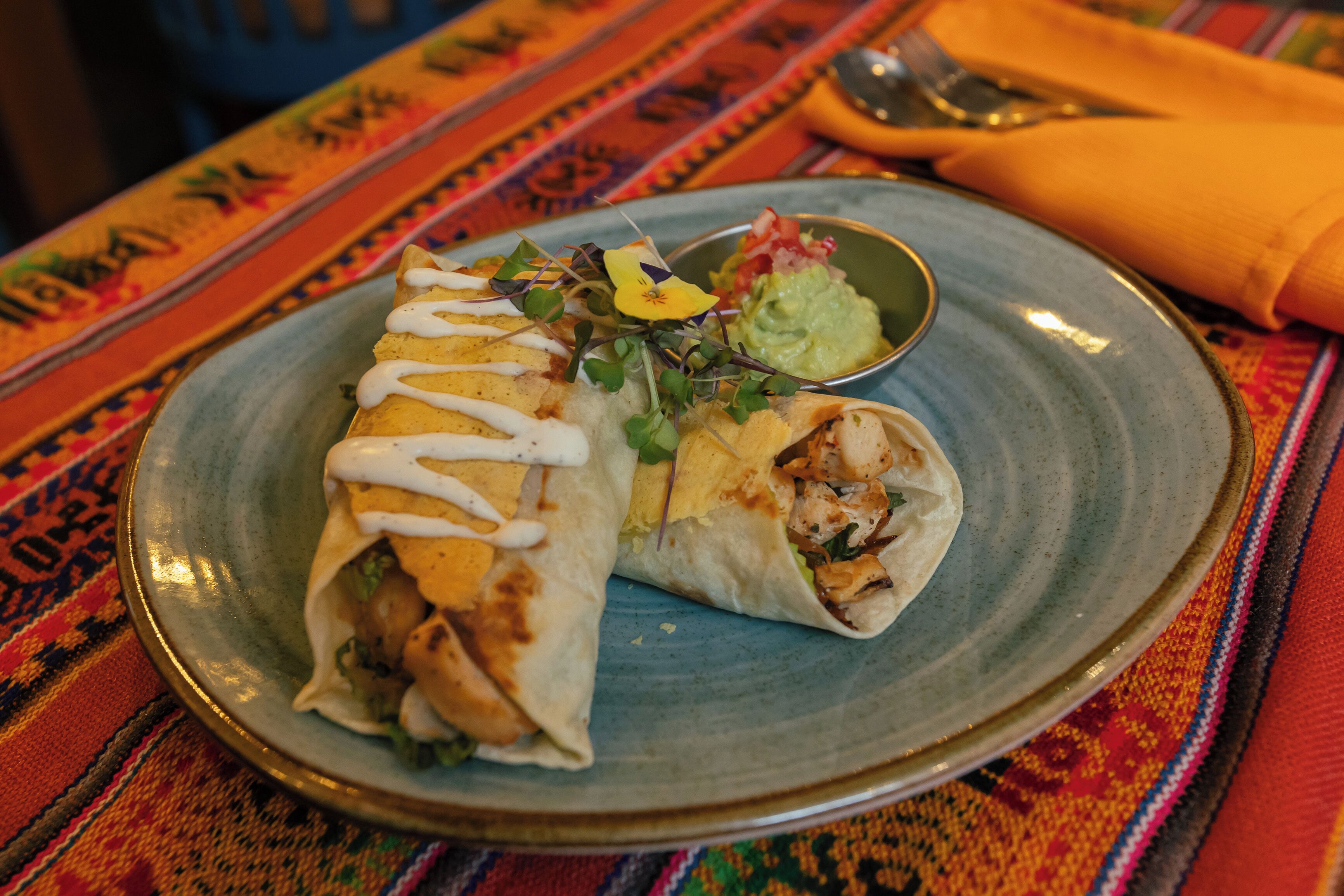 A plate with a burrito and a small bowl of guacamole.