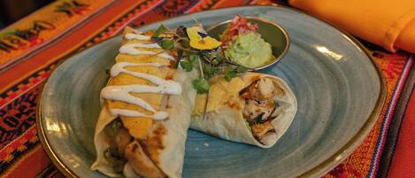 A plate with a burrito and a small bowl of guacamole.
