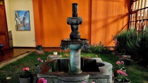 A courtyard with a stone fountain surrounded by potted plants and a painting on the wall. - Amerindia Hotel (Cusco)