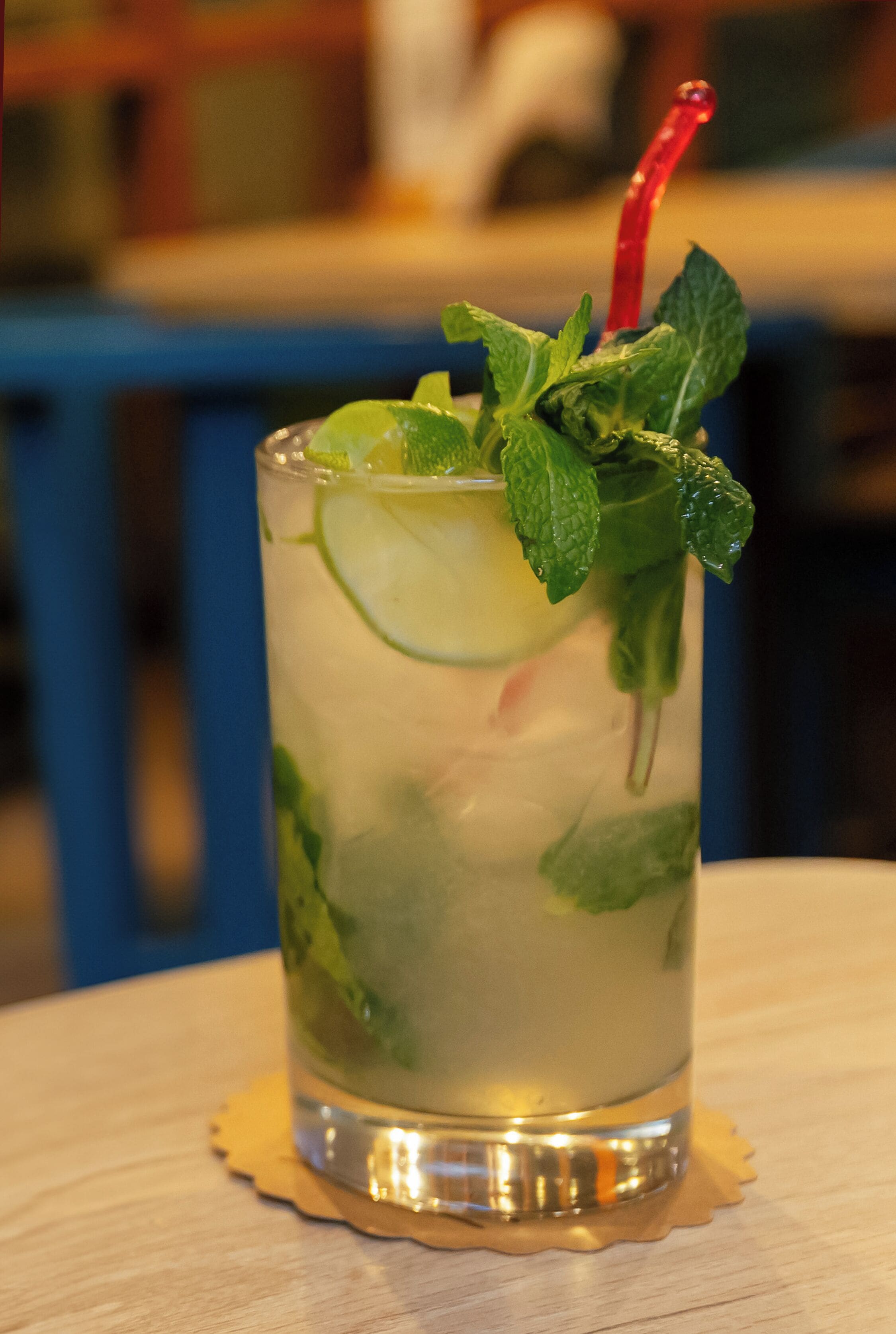 A tall glass with a lime wedge and mint leaves, placed on a coaster.