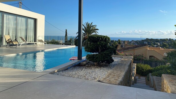 A modern outdoor pool area with lounge chairs, a view of the sea, and a clear sky. - luxurious, state-of-the-art villa with beautiful views (Denia)