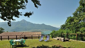 A patio with a table and chairs, overlooking a mountain and a lake.