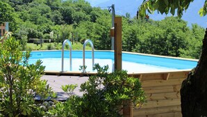 A wooden deck with a swimming pool, surrounded by greenery and trees.