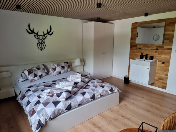 Un dormitorio moderno con una colcha de estampado geométrico, una decoración de cabeza de venado montada en la pared, un espejo grande y suelo de madera.