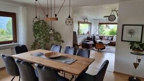A dining area with a wooden table, black chairs, hanging pendant lights, and a view of a living room with a sofa and a plant. - Modern house with unique view and 500m to the Golm ski region (Vorarlberg)